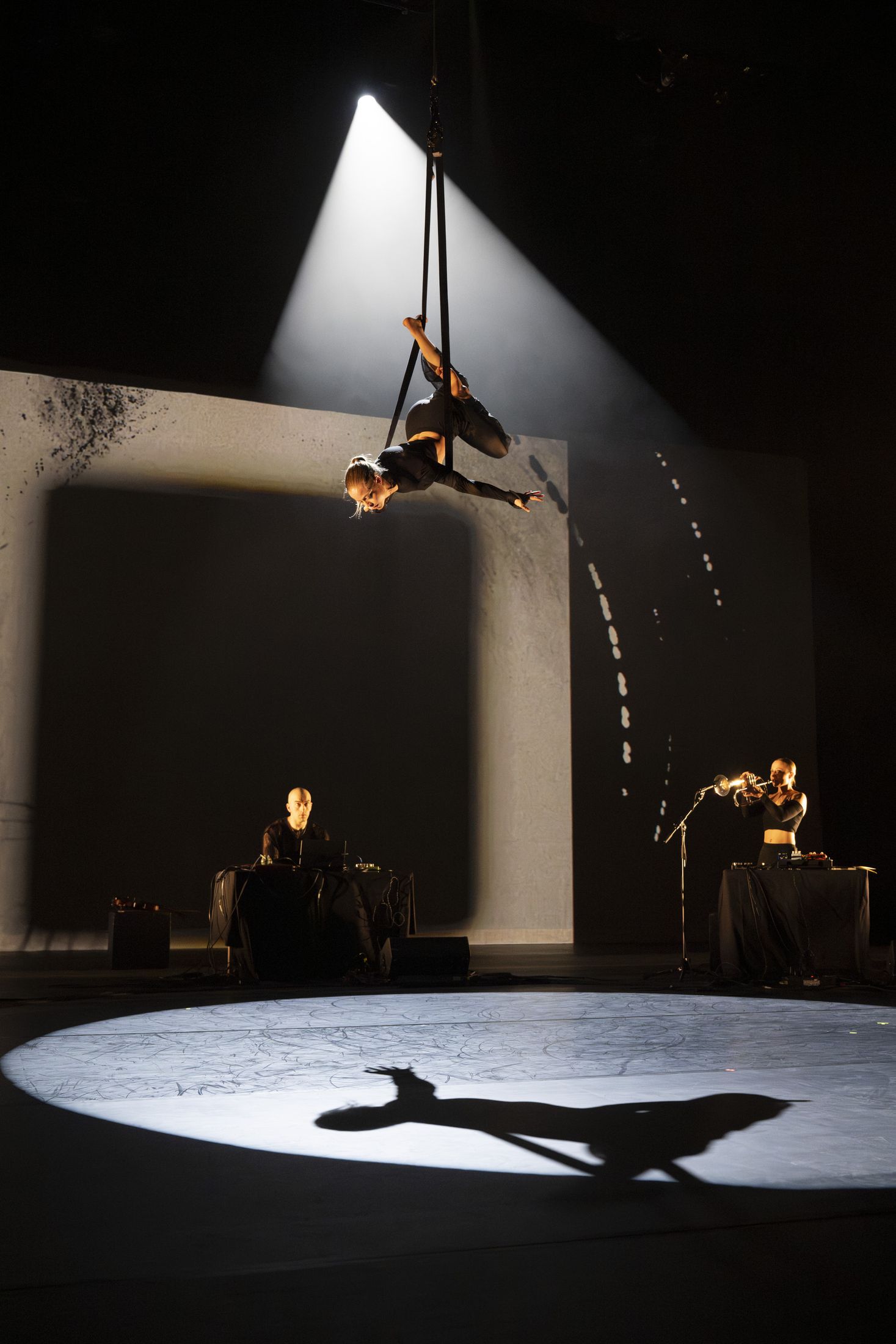 The aerialist in the beam, the trumpet at the edge of the light