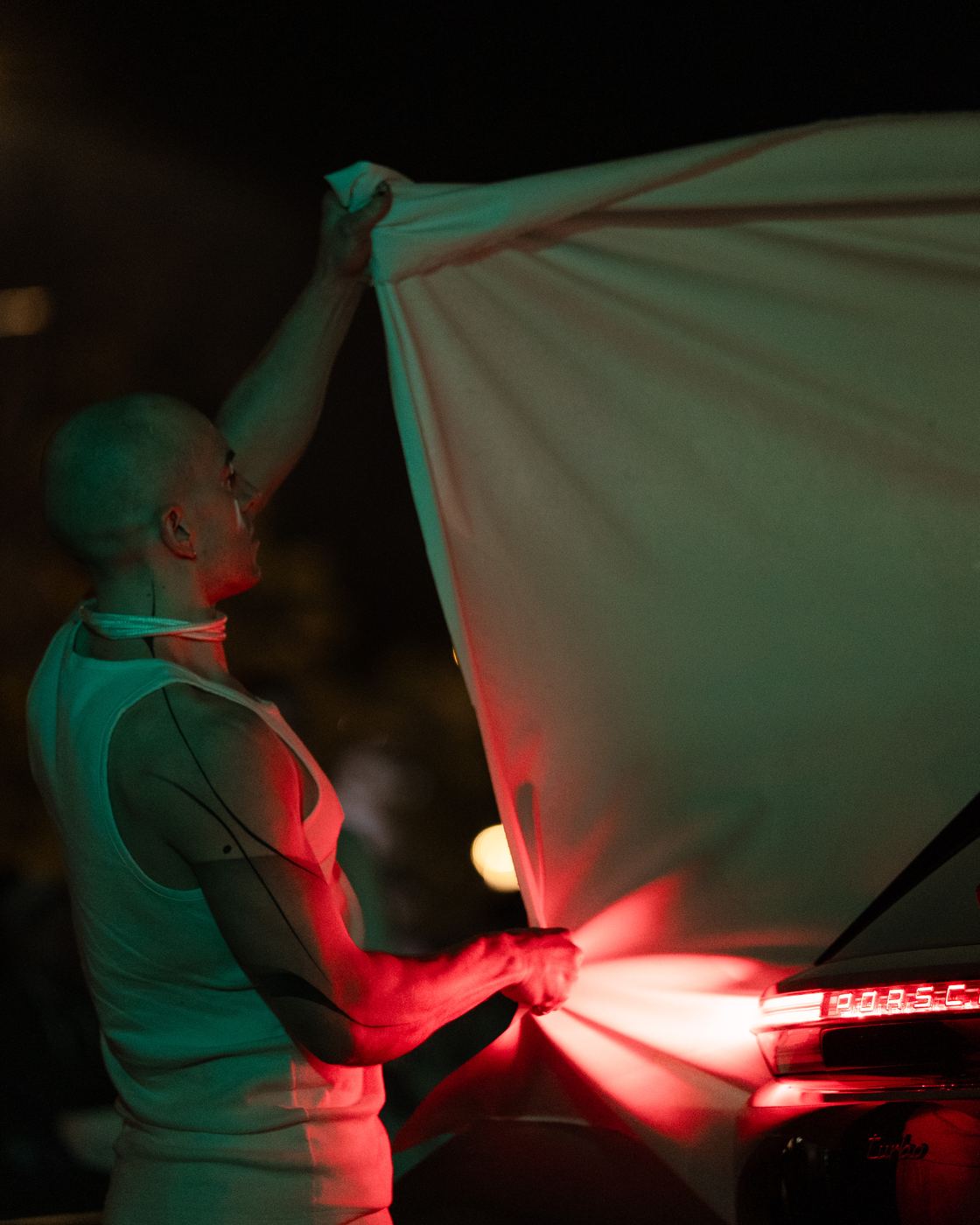 A performer pulling white fabric across the red rear light of the car