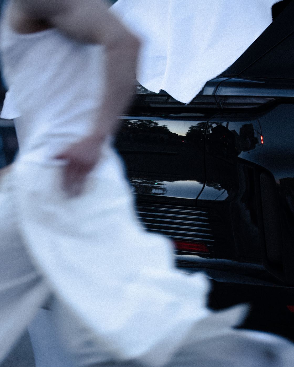 A dancer in white running past the car, blurred
