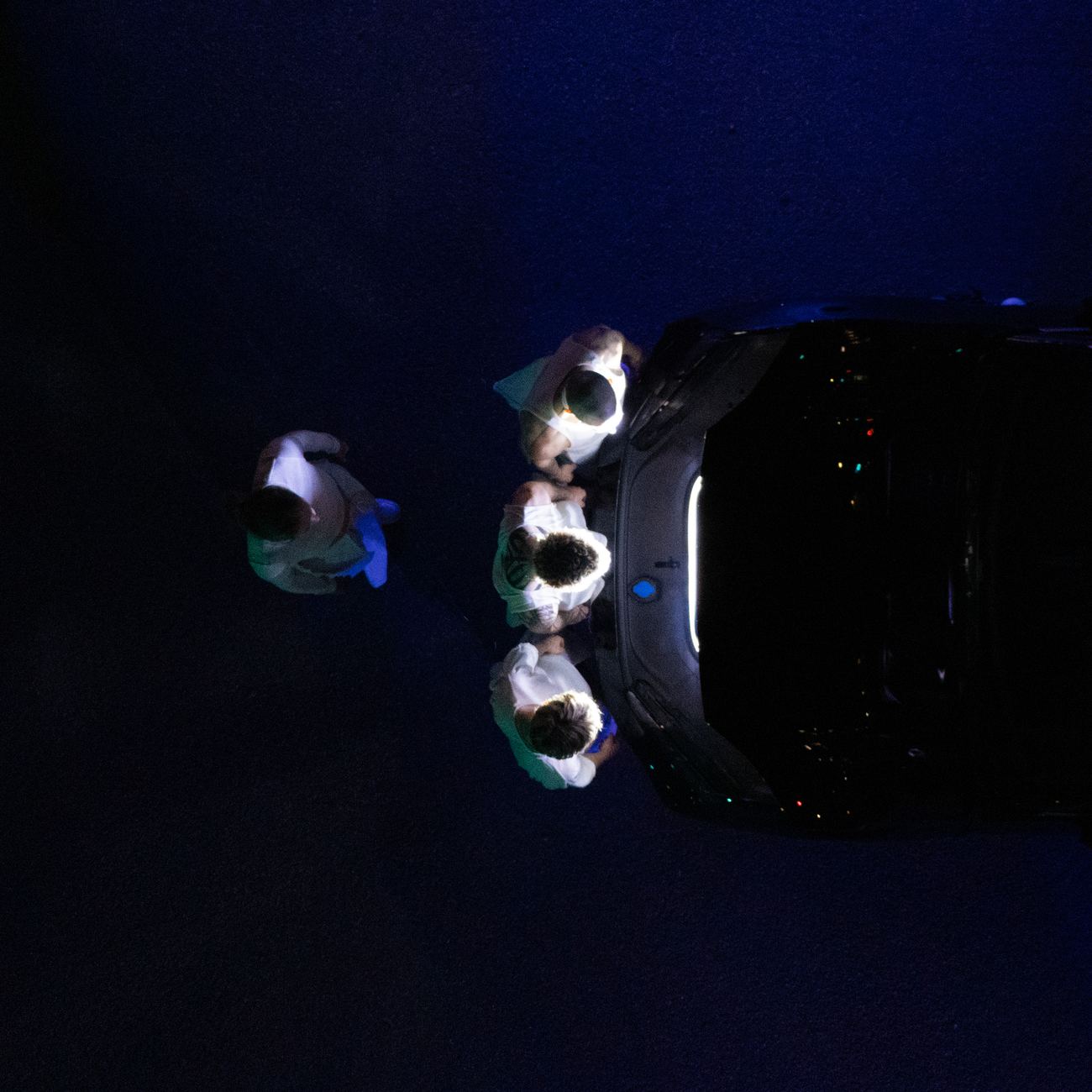 The car from directly above, performers in white gathered at its open back