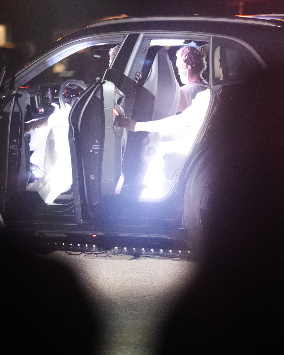 A performer inside the car, its doors open and the cabin lit